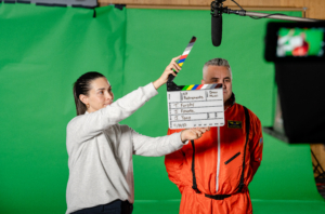 A woman holding a film slate in front of a man on camera