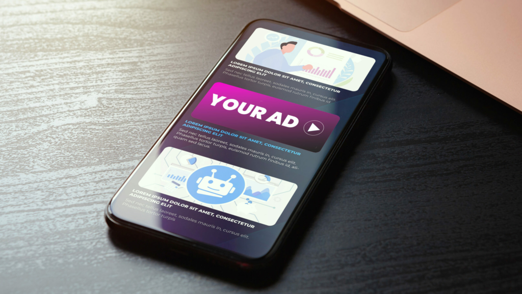 Smartphone On A Desk Displaying A ' Y O U R A D' Digital Video Ad Concept Next To A Laptop.